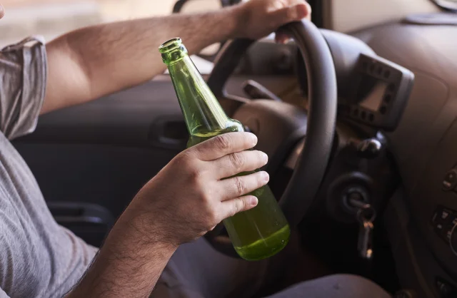 Ein Mann fährt mit Bier in der Hand Auto.